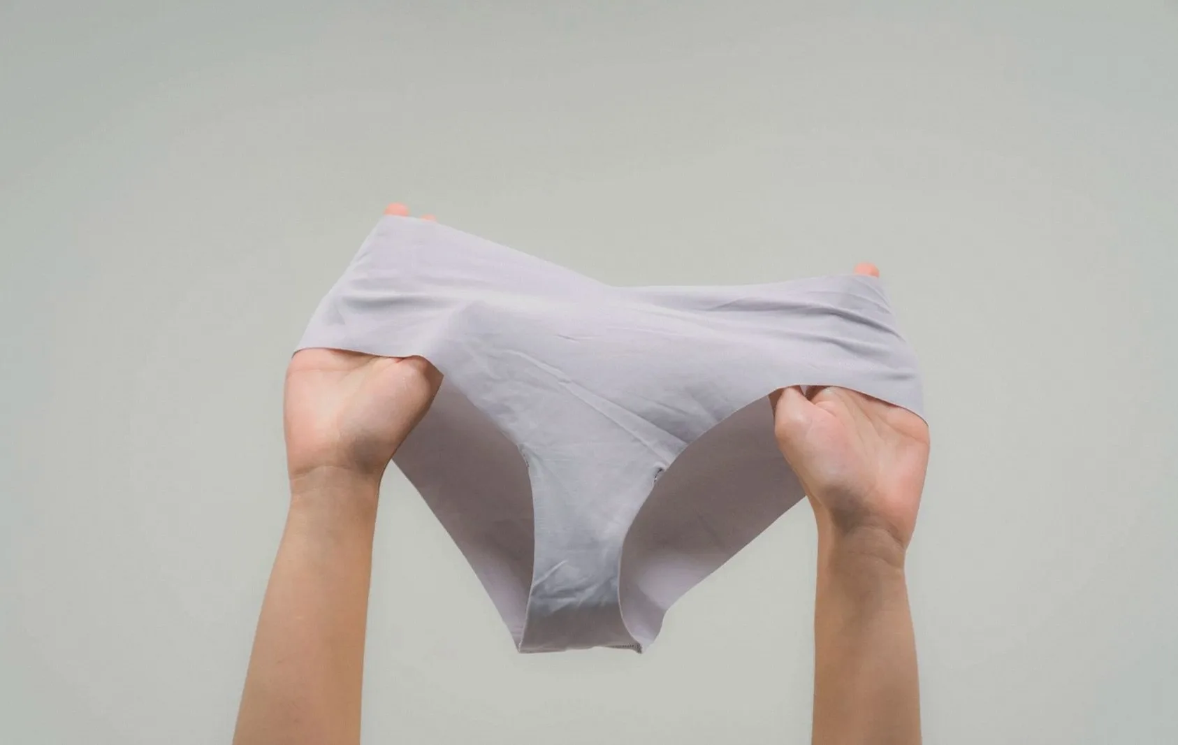 Hands stretching a pale grey brief to show the fabric